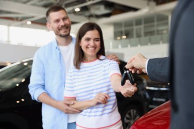 Satıcı salonda mutlu bir aileye araba anahtarı veriyor, seçici bir odak noktası.