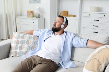 Uyum. Evdeki koltukta kulaklıkla müzik dinleyen bir adam.