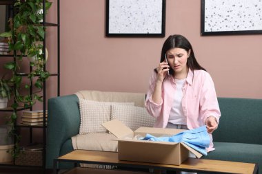 Paketi olan genç bir kadın evde telefonla müşteri hizmetlerine şikayette bulunuyor.