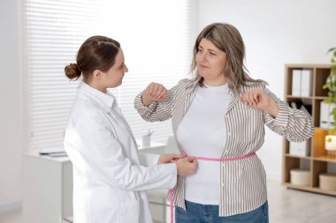 Kilo kaybı. Klinikte kilolu bir kadının belini bantla ölçen beslenme uzmanı.