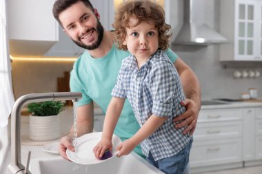 Baba ve oğlu evde birlikte bulaşık yıkıyorlar.