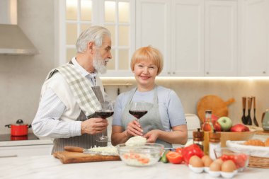 Mutfakta yemek yaparken şarap içen yaşlı çift.
