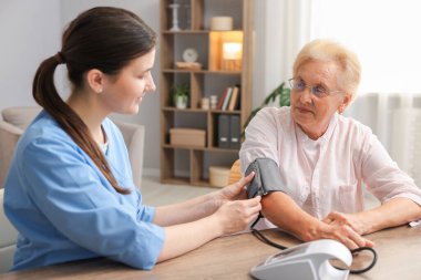 Hemşire, içeride ahşap masada hastanın kan basıncını ölçüyor. Ev sağlık hizmetleri