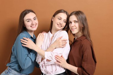 Arkadaşlar soluk kahverengi arka planda birbirlerine sarılıyorlar.