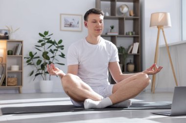 Evde bilgisayarla yoga dersi alan bir adam.