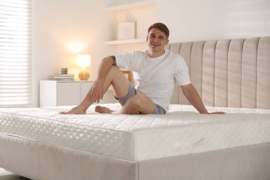 Genç adam evinde yumuşak bir yatakla yatakta oturuyor.