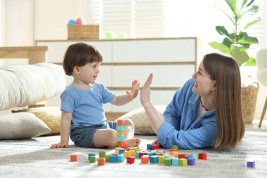 Anne ve oğul evde renkli küplerle oynarken beşlik çakıyor.