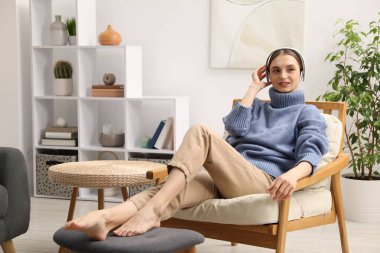 Kulaklıklı güzel bir kadın evdeki rahat koltukta dinleniyor.