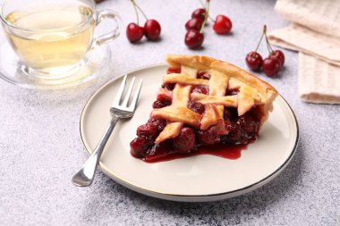 Bir parça kirazlı turta, gri desenli masada çilek ve çay, yakın plan.