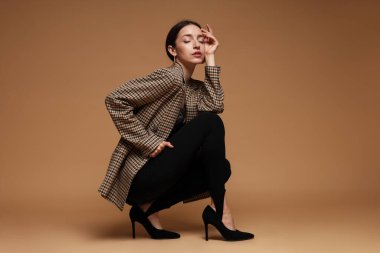 Bej arka planda şık giyinmiş güzel bir kadının tam boy portresi.