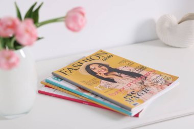 Beyaz dolaptaki birçok modaya uygun dergi ve lale çiçekleri, yakın plan.