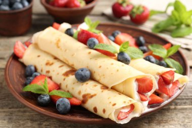 Böğürtlenli, kremalı ve naneli krepler ahşap masada, yakın plan.