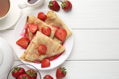 Beyaz ahşap masada çilekli leziz krepler, sos ve çay, düz yatak. Metin için boşluk