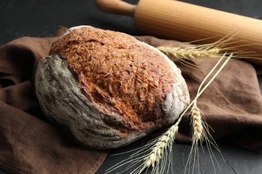 Bir somun taze ekmek, merdane ve çiviler siyah masada, yakın plan.