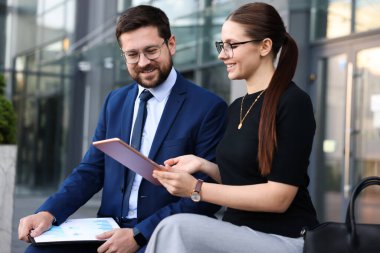 Tabletli mutlu iş arkadaşları ofis binasının yakınında bir şeyler tartışıyorlar.