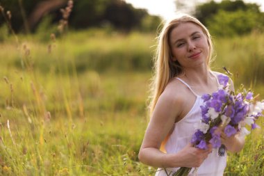 Bir buket kır çiçeğiyle güzel bir kadın çayırda güneşli bir günün tadını çıkarıyor. Metin için boşluk