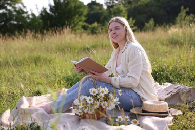 Bir buket kır çiçeğiyle çayırda kitap okuyan bir kadın.