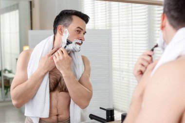 Yakışıklı adam evde aynanın yanında tıraş oluyor.