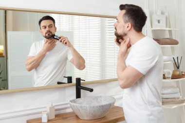 Yakışıklı adam evde aynanın yanında tıraş makinesiyle tıraş oluyor.