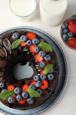 Hafif ahşap masada çilekli, nane ve böğürtlenli lezzetli çikolatalı kek.