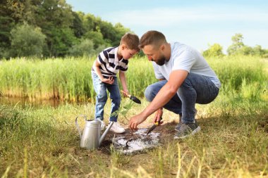 Baba ve oğlu dışarıda toprağa ağaç dikiyorlar.