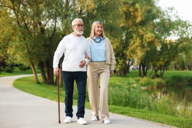 Parkta göl kenarında birlikte yürüyen sevimli yaşlı çift.