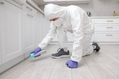 Koruyucu kıyafetli haşereci evde böcek ilacı sıkıyor.