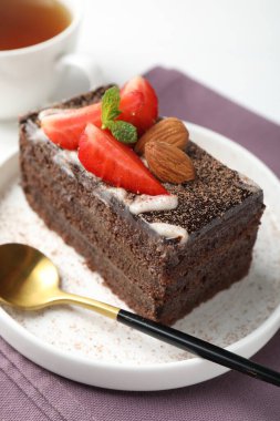 Çilekli, bademli ve masada çay bulunan bir dilim lezzetli çikolatalı pasta.