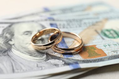 İki altın alyans ve bir dolarlık banknotlar beyaz masada, yakın plan.