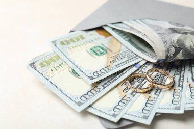 İki altın alyans, bir dolarlık banknotlar ve beyaz masanın üzerindeki zarf, yakın plan.