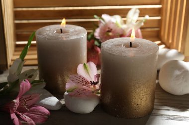 Yakıcı mumlar, taşlar ve zambak çiçekleri ahşap masada, yakın plan