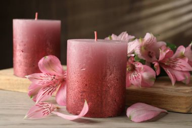 Güzel mumlar ve zambak çiçekleri beyaz ahşap masada, yakın plan.