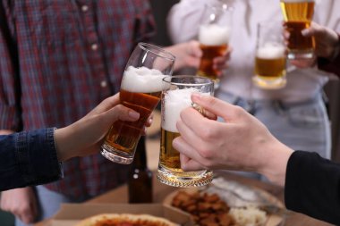 Arkadaşlar masada bira bardaklarını tokuşturur, yakın plan