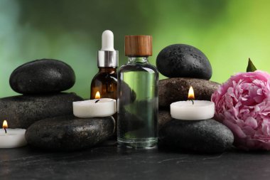 Islak taşlı spa kompozisyonu, kozmetik ürünleri ve koyu desenli masada yanan mumlar, bulanık yeşil arka plan, yakın çekim