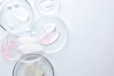 Petri kabında farklı kozmetik ürünleri, beyaz arka planda, düz yerde. Metin için boşluk