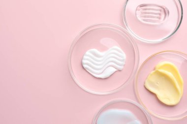 Petri kaplarında pembe arka planda farklı kozmetik ürünleri var. Metin için boşluk