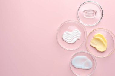 Petri kaplarında pembe arka planda farklı kozmetik ürünleri var. Metin için boşluk