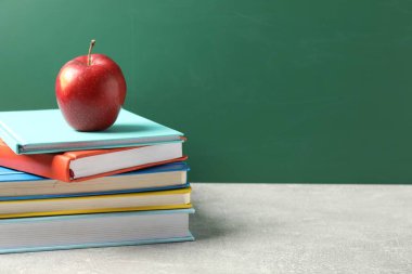 Farklı kitaplar ve gri masada kırmızı elma tahtaya karşı, yakın plan. Metin için boşluk