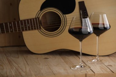 Akustik gitar ve ahşap masada kırmızı şarap kadehleri. Metin için boşluk