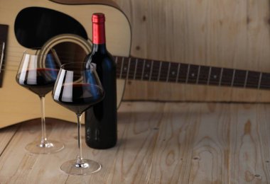 Akustik gitar, şişe ve kırmızı şarap bardakları ahşap masada. Metin için boşluk
