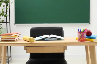 Farklı okul kırtasiyesi ve tahtanın yanındaki ahşap masada kırmızı elma.