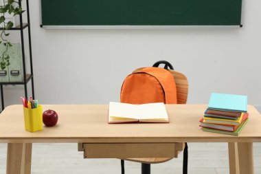 Farklı okul kırtasiyesi ve kırmızı elma, kapalı alanda tahtaya yakın ahşap masada.