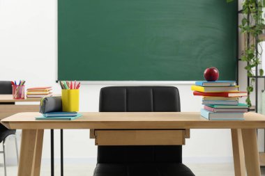 Farklı okul kırtasiyesi ve kırmızı elma, kapalı alanda tahtaya yakın ahşap masada.