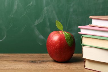 Tahtanın yanındaki ahşap masada farklı kitaplar ve kırmızı elma, yakın plan. Metin için boşluk