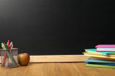 Tahtanın yanındaki ahşap masada farklı kırtasiye ve elma, metin için yer