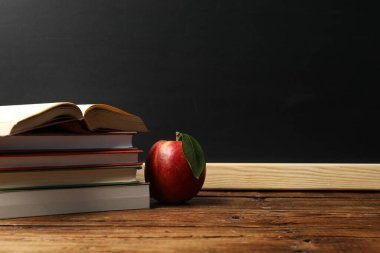 Tahtanın yanındaki ahşap masada farklı kitaplar ve kırmızı elma, metin için yer.