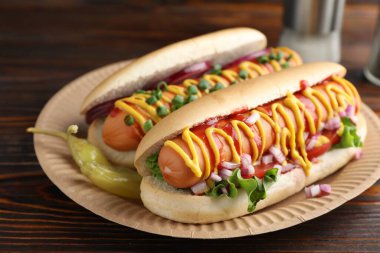 Ahşap masada soslu, marullu ve soğanlı lezzetli sosisliler, yakın plan.