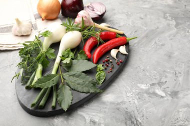 Farklı taze otlar, sarımsak, soğan ve diğer baharatlar gri masada, yakın plan. Metin için boşluk