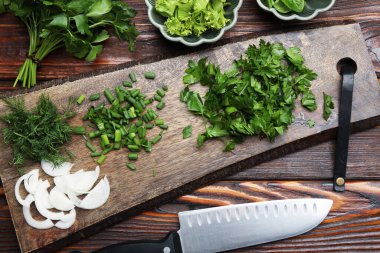 Farklı taze otlar, baharatlar ve bıçaklar ahşap masada, düz yerde.