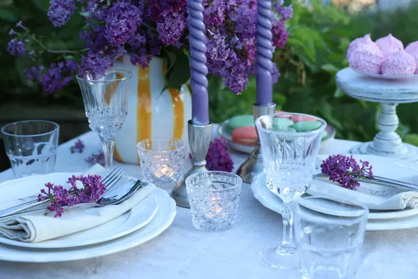 Güzel leylak çiçekleri, tabaklar, çatal bıçaklar, bardaklar ve mumlar bahçede, yakın plan.